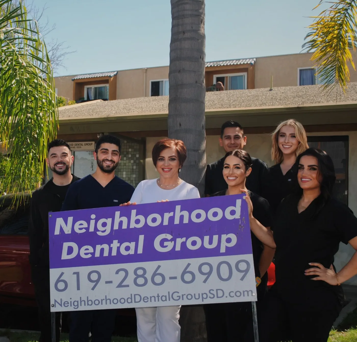 The Neighborhood Dental Group team outside the office holding a sign with the practice name and phone number
